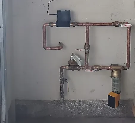 A smart water shutoff valve on a copper main-line manifold with a pressure-reducing valve and a whole-house filter, mounted on a garage wall